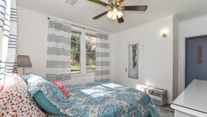 Un dormitorio con cama, ventilador de techo, ventana con cortinas, cómoda y puerta con un letrero.