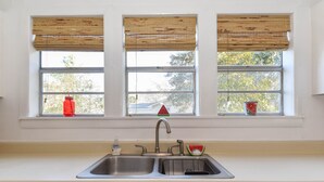 Una cocina con un lavamanos doble, persianas de madera y un ventanal con un objeto rojo y un florero.