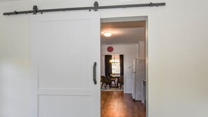 Un pasillo con una puerta corredera que da a un comedor con una araña y un reloj en la pared.