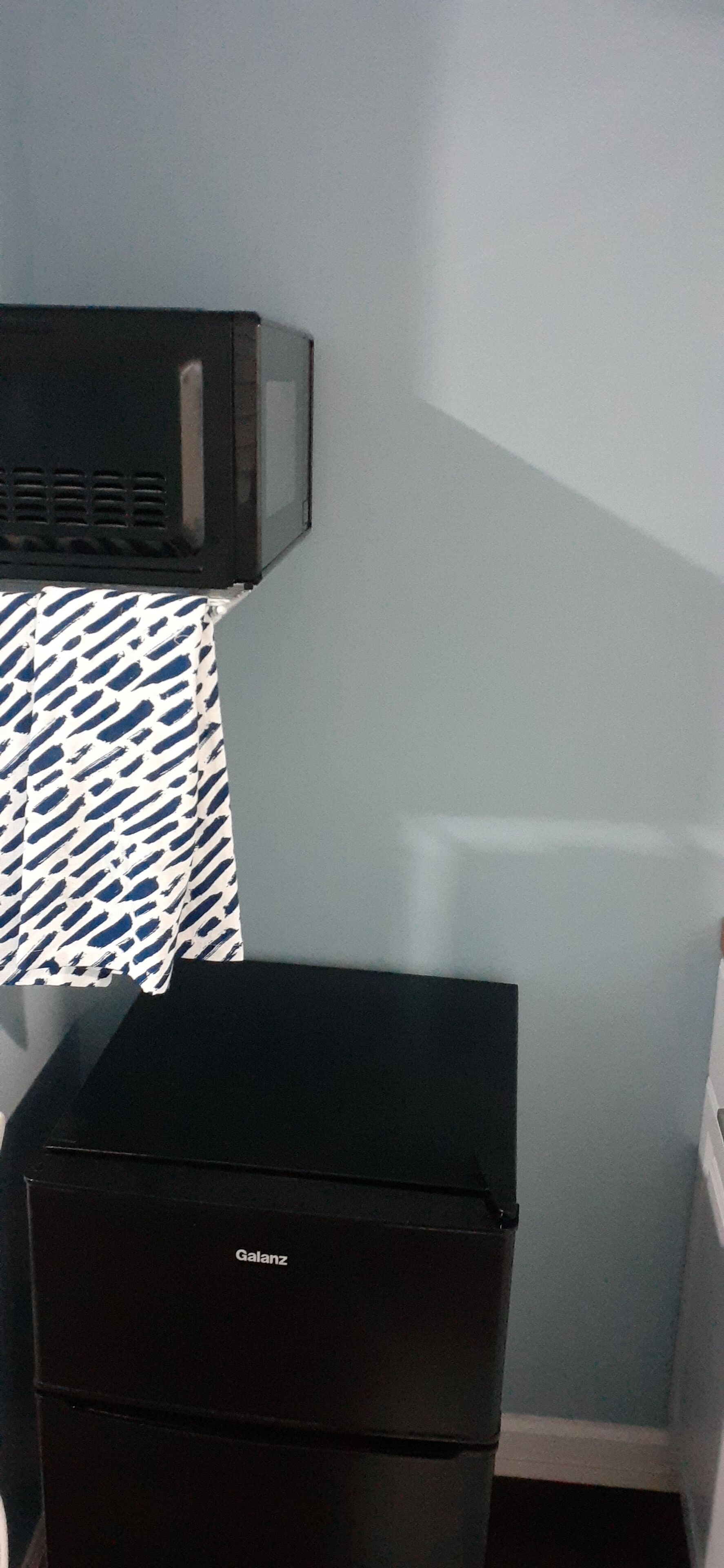 Ein schwarzes Gerät mit dem Markennamen 'Galanz', eine gemusterte Tischdecke und eine hellblaue Wand.