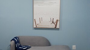Un soggiorno con un divano grigio, una parete blu e un quadro a tema spiaggia.