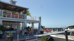 Un edificio moderno con una terraza en la azotea, mobiliario exterior y vistas al puerto deportivo.