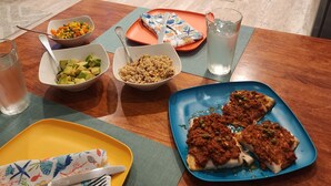 Una mesa de comedor con diversos platos, como pizza y ensaladas, en una cocina moderna con armarios blancos y electrodomésticos de acero inoxidable.