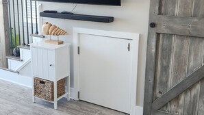 Una sala de estar moderna con un televisor de pantalla plana montado en la pared, un mueble blanco con una cesta tejida y una puerta de madera rústica.
