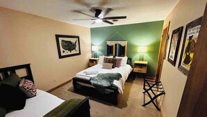 Une chambre avec deux lits, un ventilateur de plafond et des tableaux encadrés accrochés aux murs.