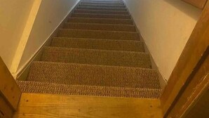 Un escalier étroit avec des rampes en bois, menant à une petite fenêtre située en haut.
