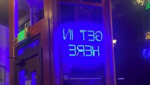 Une enseigne au néon indiquant « SORTIE » et « SORTIE PAR ICI » dans un restaurant, avec une table et un verre de bière.