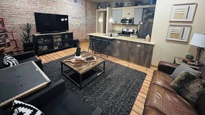 Un salon moderne avec un mur en briques, un téléviseur à écran plat, une table basse en bois et un canapé en cuir.
