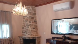 Una sala de estar acogedora con chimenea de piedra, un candelabro, una mesa de comedor con sillas y un televisor montado en la pared.