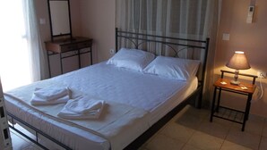 Una cama bien tendida con sábanas y toallas blancas, una mesita de noche con una lámpara, un espejo y un atril de madera.