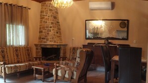 Una sala de estar acogedora con chimenea de piedra, un sofá, una mesa de comedor y una araña.