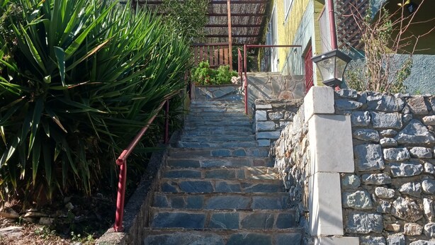 Una escalera de piedra que sube hacia un edificio con barandilla roja y pared de piedra.