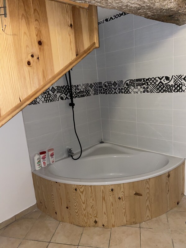 Een badkamer op de hoek met een houten bad, een douche en een betegelde muur met decoratieve rand.
