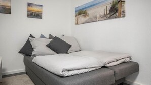 A neatly made bed with grey bedding and pillows, a grey sofa, and a wall with three framed pictures. - Vacation apartment Heide II (Walsrode)