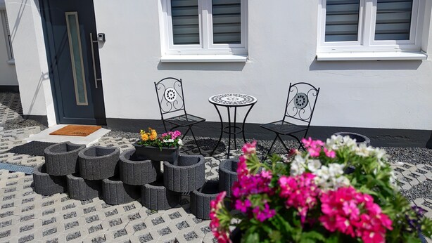 A patio with two metal chairs and a small round table, a door, and two windows with shutters. - Vacation apartment Heide II (Walsrode)