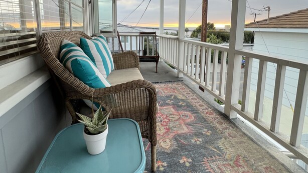 A covered porch with a wicker sofa, a small table with a plant, and a patterned rug. - Ocean View 2 Bedroom 1 Bath Sunny clean Apartment (Laguna Beach)