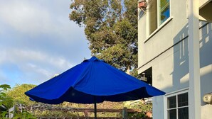 A patio with a round table and four chairs, a blue umbrella, and a wooden fence in the background. - Ocean View 2 Bedroom 1 Bath Sunny clean Apartment (Laguna Beach)