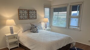 A neatly arranged bedroom with a bed, two bedside tables with lamps, a decorative wall piece, and a window with blinds. - Ocean View 2 Bedroom 1 Bath Sunny clean Apartment (Laguna Beach)