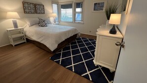 A bedroom with a bed, nightstands, a dresser, a window with blinds, and a door. - Ocean View 2 Bedroom 1 Bath Sunny clean Apartment (Laguna Beach)