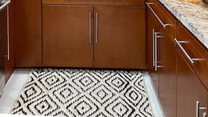 Une cuisine avec des meubles en bois, un plan de travail en granit, un évier encastré et un tapis à motifs.