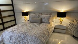 Une chambre à coucher avec un grand lit, deux tables de chevet avec des lampes, une tête de lit et une étagère fixée au mur.