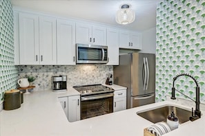 Enjoy cooking in this well-equipped kitchen with a stainless steel refrigerator, oven, and patterned backsplash.