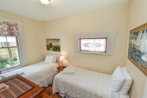 A room with two single beds, a small table, a lamp, and a window with a view of greenery. - Artist House Lower in Forsyth Park Neighborhood Hist Savannah (Savannah)