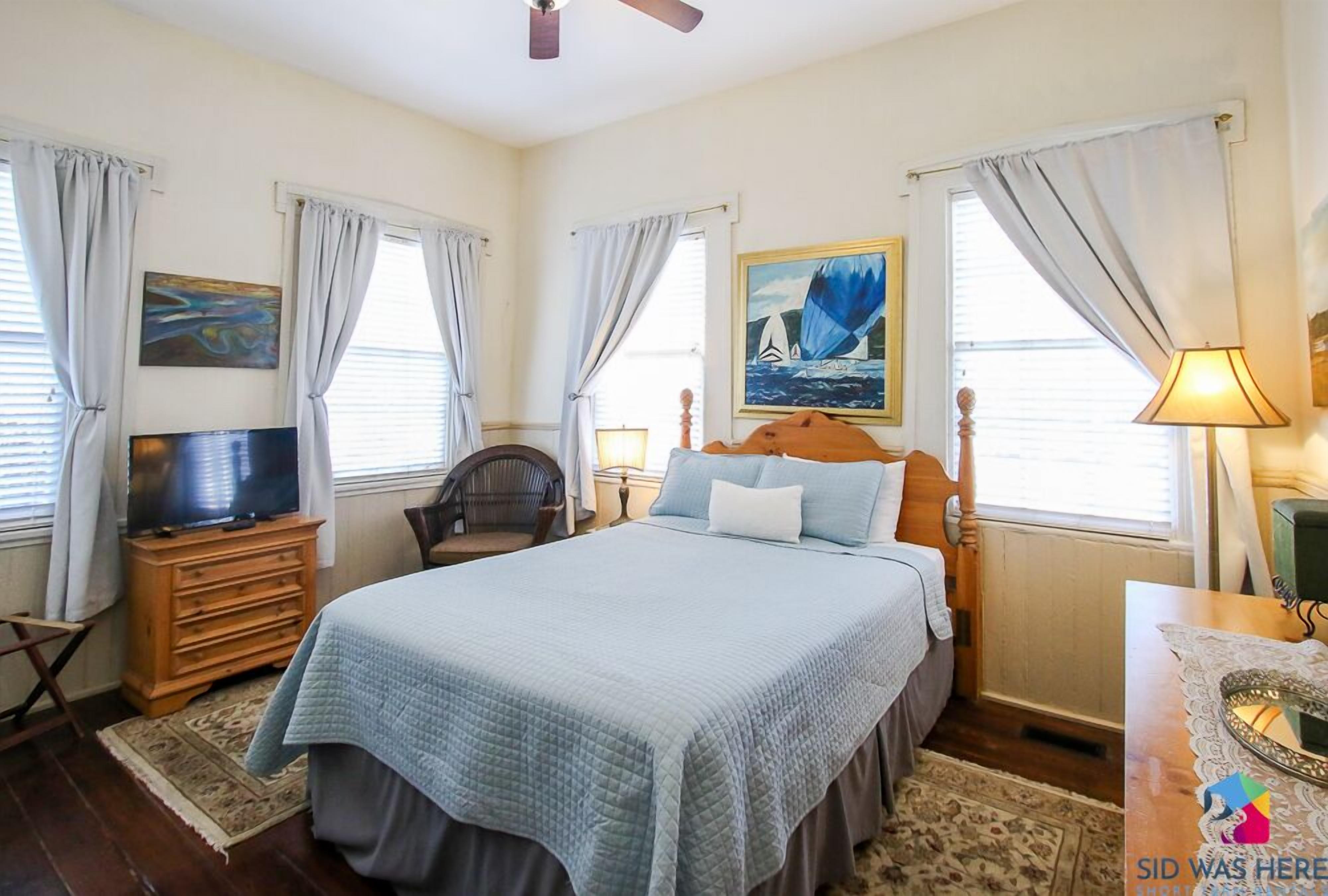 A bedroom with a bed, a television, a chair, a desk, and a lamp.