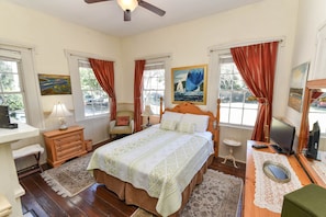 Quarto com cama, escrivaninha, cadeira, abajur e um quadro na parede.