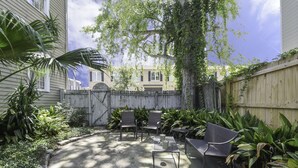 Ein Garten mit Holzzaun, einer Terrasse mit Stühlen und Tisch sowie verschiedenen Pflanzen.