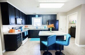 A modern kitchen with dark cabinets, a central island with blue bar stools, a microwave, and a refrigerator. - Cozy 3 bedroom, Centrally Located, Perfect for a family (Montgomery)