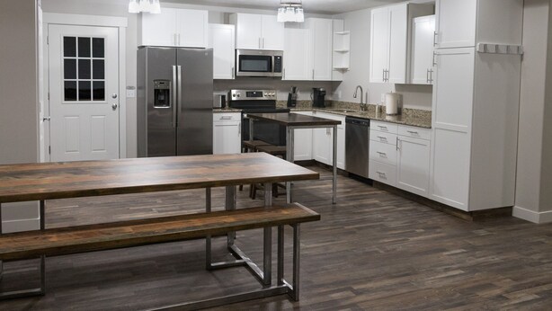 A modern kitchen with white cabinets, stainless steel appliances, and a wooden dining table. - New home sleeps 10, open floor plan & amazing view (Manila)