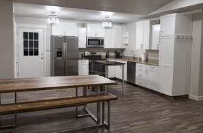 Une cuisine moderne avec des meubles blancs, des appareils en acier inoxydable et une table à manger en bois.