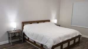 A bedroom with a wooden bed frame, white bedding, and two bedside tables with lamps. - New home sleeps 10, open floor plan & amazing view (Manila)
