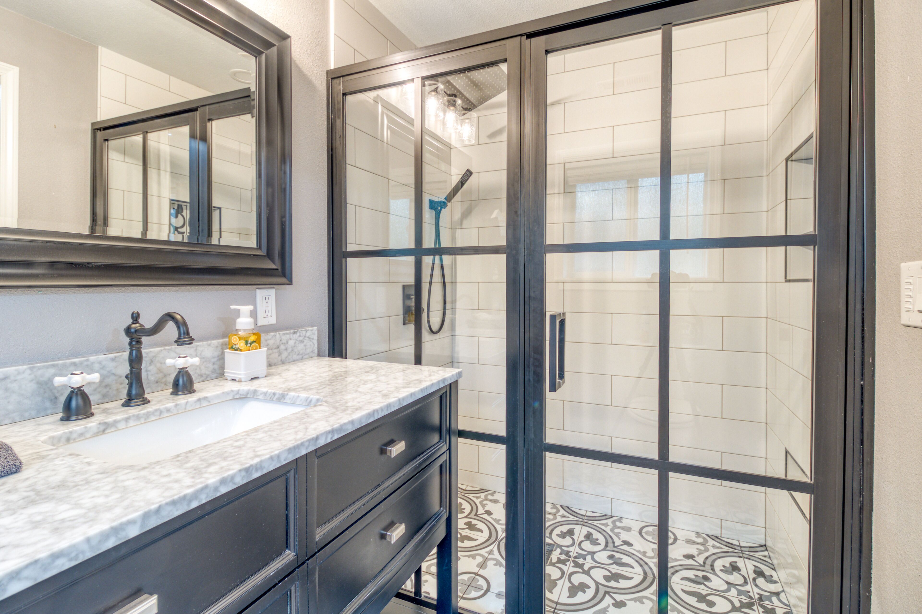 A bathroom with a glass shower enclosure, a sink with a marble countertop, and a mirror above the sink.