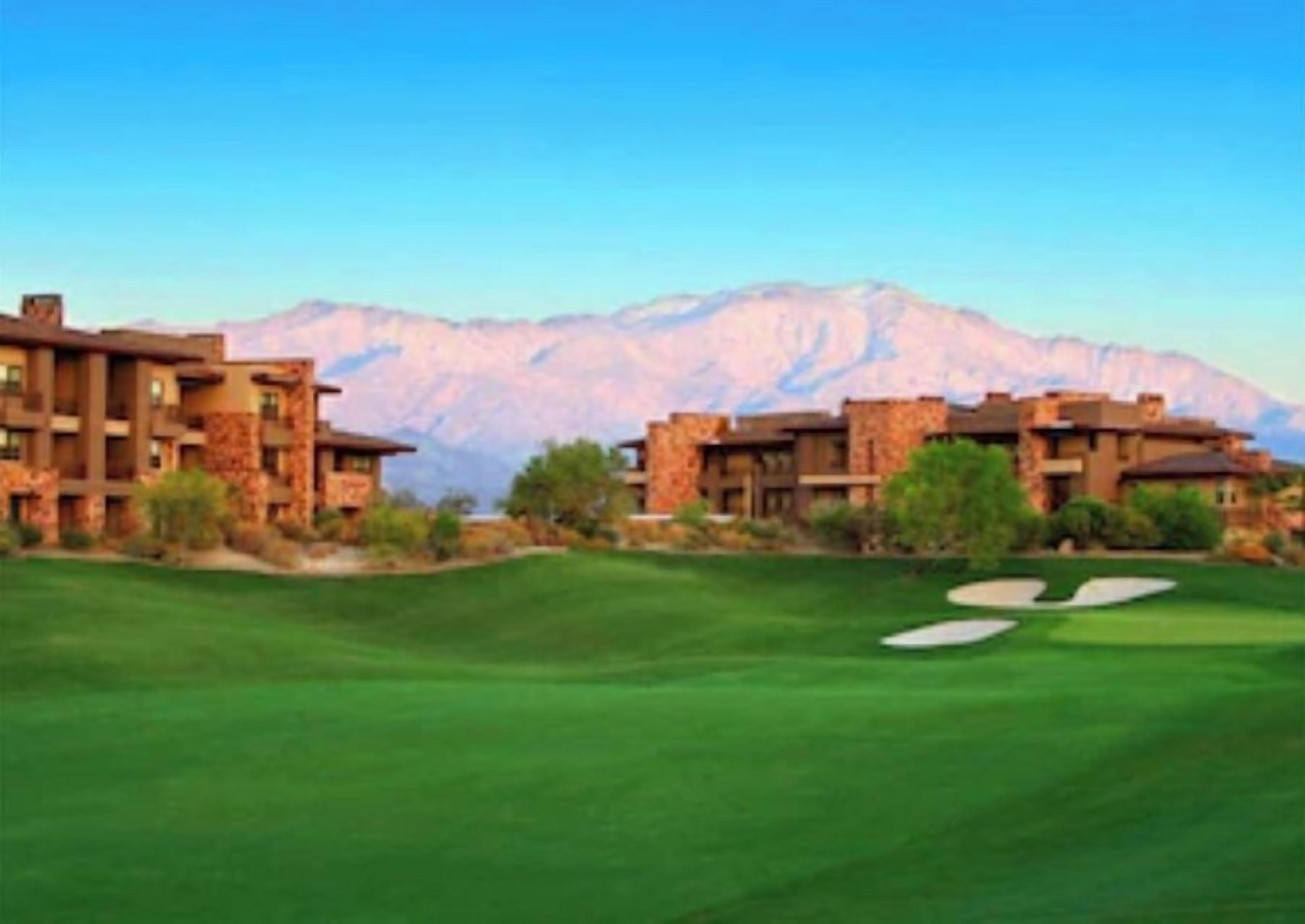 A golf course with a mountain backdrop and a building with multiple floors and balconies.