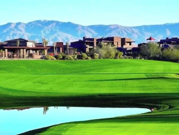Un parcours de golf avec un étang, des maisons en arrière-plan et des montagnes.