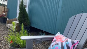 Un petit bâtiment d’un seul étage, à la façade de couleur turquoise, doté d’une terrasse en bois et d’une chaise agrémentée d’un coussin aux couleurs vives.