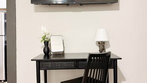 A modern room with a flat-screen TV mounted on the wall, a desk with a chair, a vase with flowers, and a lamp. - Suite Home Indiana #2 (Evansville)