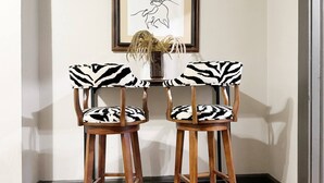 A dining area with two wooden chairs with zebra-patterned cushions, a framed artwork on the wall, and a vase with dried flowers on the table. - Suite Home Indiana #2 (Evansville)