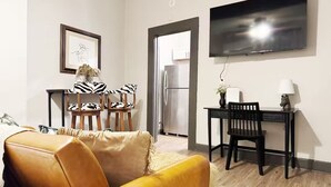 A modern living room with a leather sofa, a zebra-patterned chair, a dining table with chairs, a flat-screen TV mounted on the wall, and a refrigerator in the background. - Suite Home Indiana #2 (Evansville)