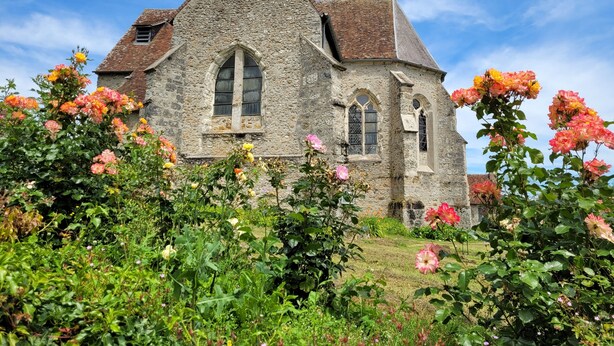 A stone building with a triangular roof and arched windows, surrounded by lush gardens and flowering plants. - Gîte Grande Capacité in Champagne (Verdon)