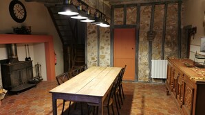 A rustic dining area with a wooden table and chairs, a stone wall, and a staircase leading to an upper level. - Gîte Grande Capacité in Champagne (Verdon)