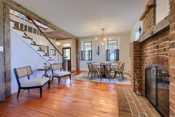 A spacious living area with a wooden staircase, a fireplace, and a dining table with chairs.