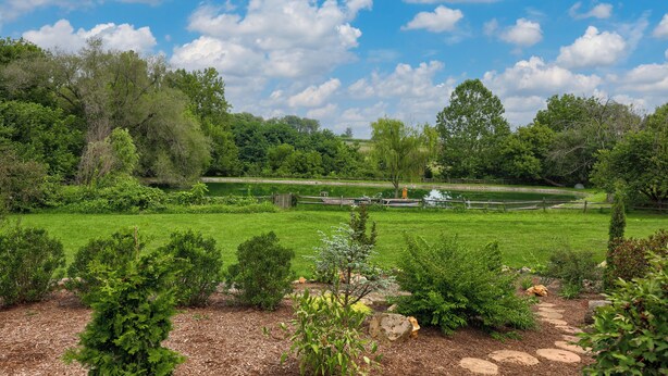 A lush garden with a variety of trees and shrubs, a clear blue sky, and a pond in the background. - The Tannery  
A swanky, eclectic and fun adult retreat. (Lancaster)