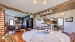 A spacious dining area with a marble table and wooden chairs, a kitchen in the background, and a staircase leading to another level. - The Tannery  
A swanky, eclectic and fun adult retreat. (Lancaster)