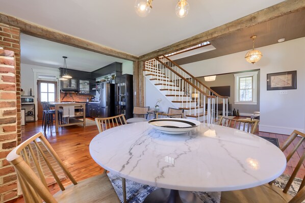 A spacious dining area with a marble table and wooden chairs, a kitchen in the background, and a staircase leading to another level. - The Tannery  
A swanky, eclectic and fun adult retreat. (Lancaster)