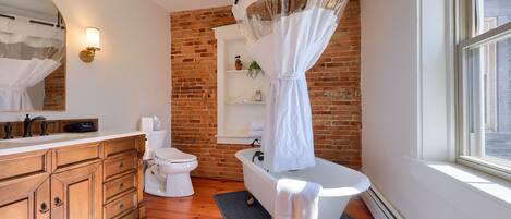 Un baño con una bañera blanca, un tocador de madera, un inodoro blanco y una pared de ladrillo.