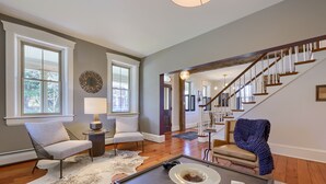 A spacious living room with a wooden floor, a large window, a staircase, and a cozy seating area. - The Tannery  
A swanky, eclectic and fun adult retreat. (Lancaster)