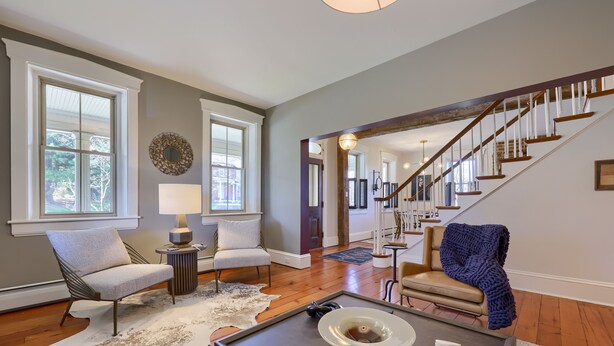 A spacious living room with a wooden floor, a large window, a staircase, and a cozy seating area.